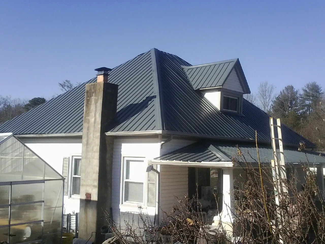 Dark blue standing seam metal roof on a white farmhouse with dormer — Slate & Tile Roof Repair by Roofing Brothers in Mayesville