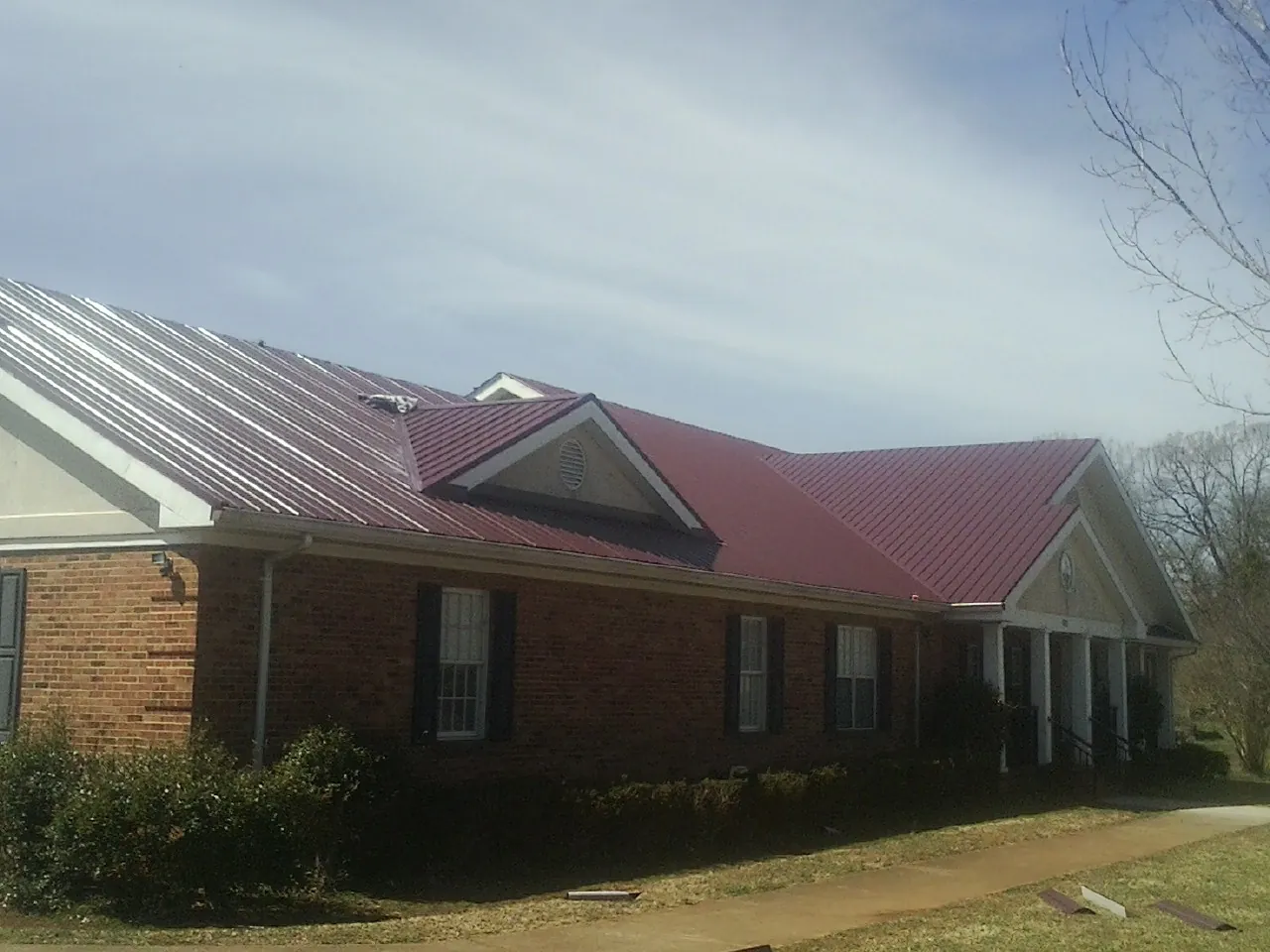 Red metal roof with gabled entries on a long brick building, from a Hail Damage Roof Repair job in Mayesville