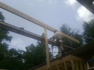 Carpenter setting a ridge beam over a new addition frame in Mayesville