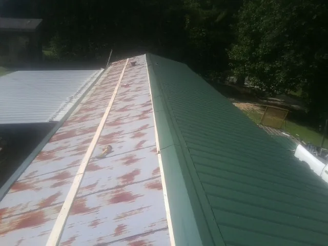 Old rusted panels beside newly installed green metal roofing — Wind Damage Roof Repair by Roofing Brothers in Mayesville