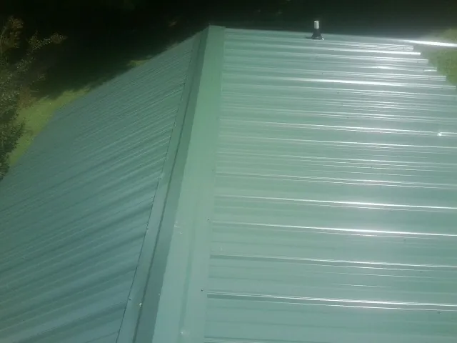 New green metal panels meeting at the ridge of a roof — Flat Roof Repair work by our crew in Mayesville