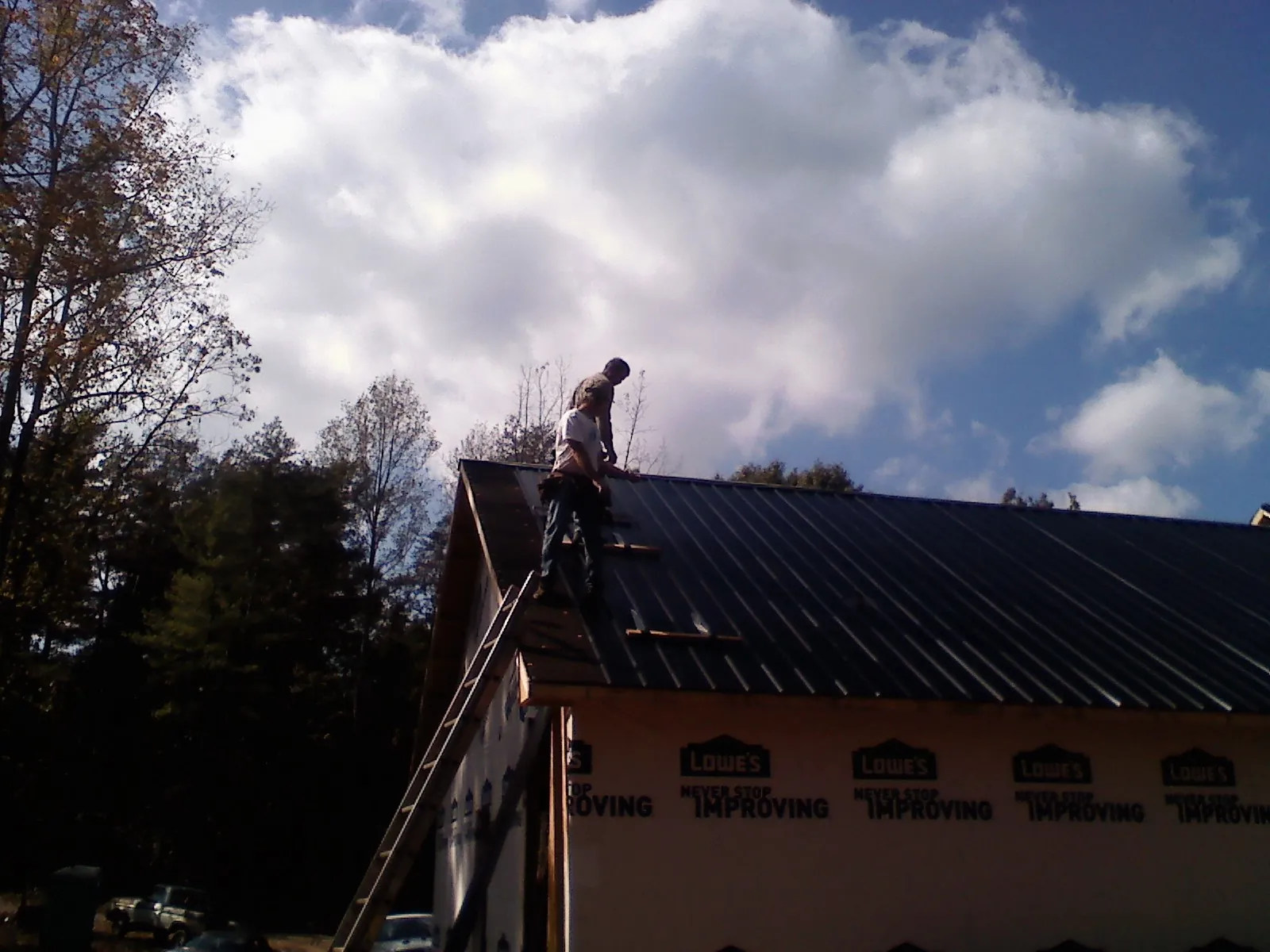 Roofer fastening dark metal panels high against a cloudy sky, from a Roof Inspection job in Mayesville